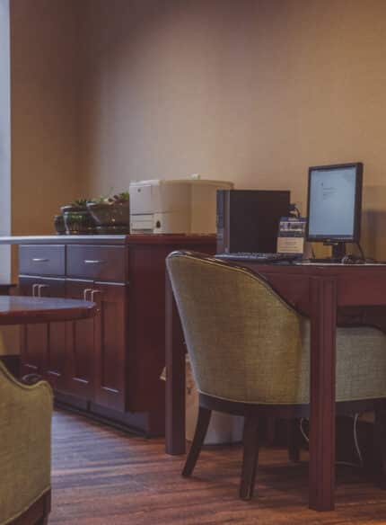 Office corner with a desk, chair, computer, printer, and cabinets under a large window.