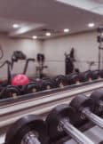 A gym with free weights in the foreground, treadmills, stationary bikes, and a cable machine in the background.